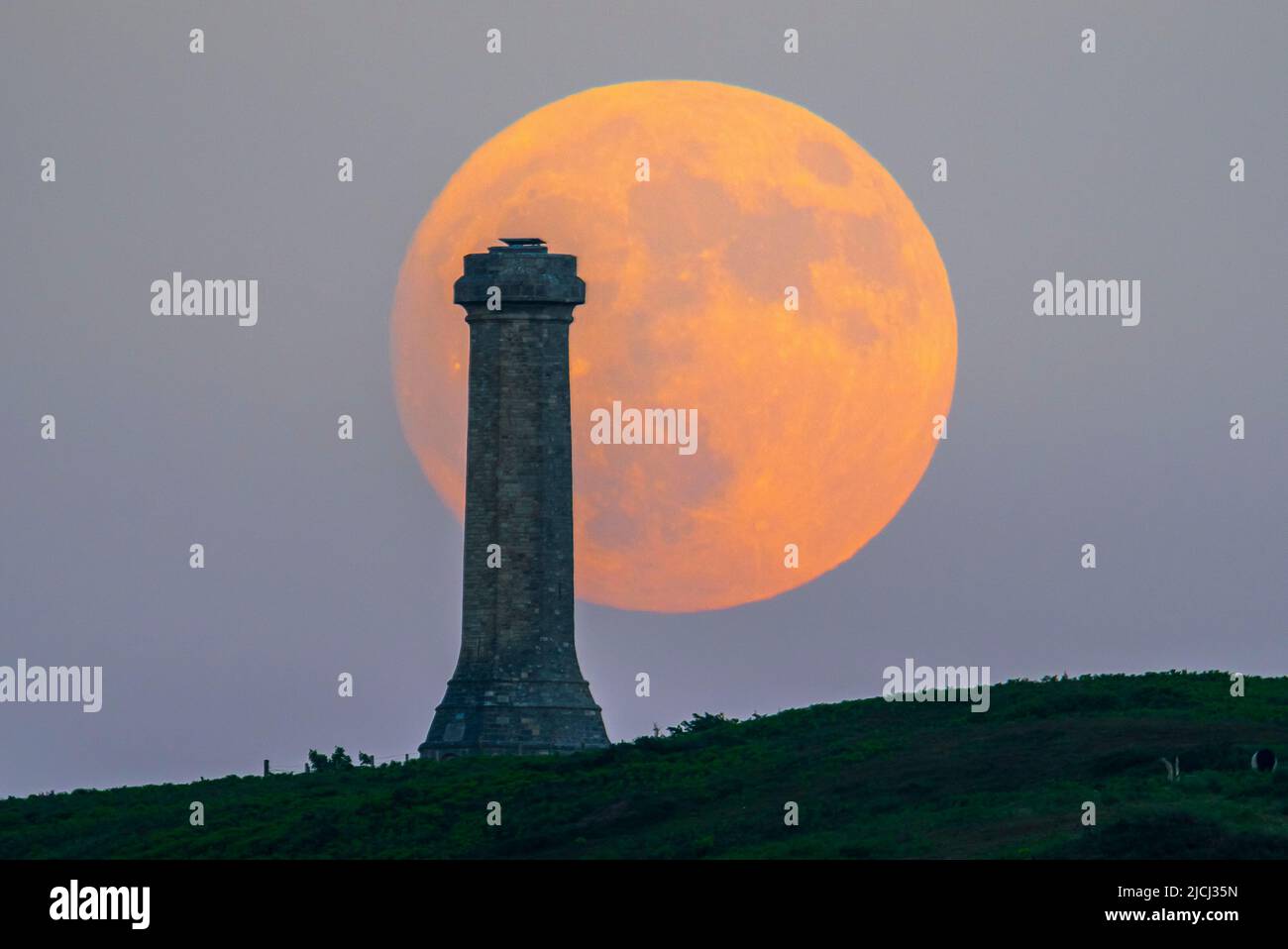 Portesham, Dorset, Großbritannien. 13.. Juni 2022. Wetter in Großbritannien. Der fast volle Strawberry Super Moon leuchtet orange, als er sich hinter dem Hardy Monument in Portesham in Dorset erhebt. Das Denkmal wurde 1844 in Erinnerung an den Vizeadmiral Sir Thomas Masterman Hardy errichtet, der Flaggenkapitän der HMS Victory bei der Schlacht von Trafalgar war. Bildnachweis: Graham Hunt/Alamy Live News Stockfoto