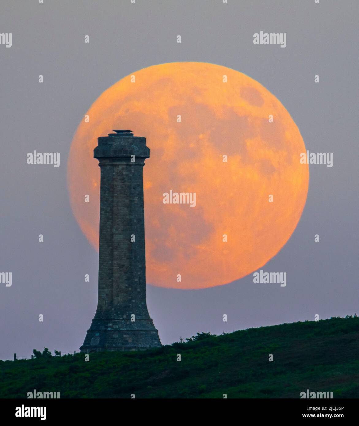 Portesham, Dorset, Großbritannien. 13.. Juni 2022. Wetter in Großbritannien. Der fast volle Strawberry Super Moon leuchtet orange, als er sich hinter dem Hardy Monument in Portesham in Dorset erhebt. Das Denkmal wurde 1844 in Erinnerung an den Vizeadmiral Sir Thomas Masterman Hardy errichtet, der Flaggenkapitän der HMS Victory bei der Schlacht von Trafalgar war. Bildnachweis: Graham Hunt/Alamy Live News Stockfoto