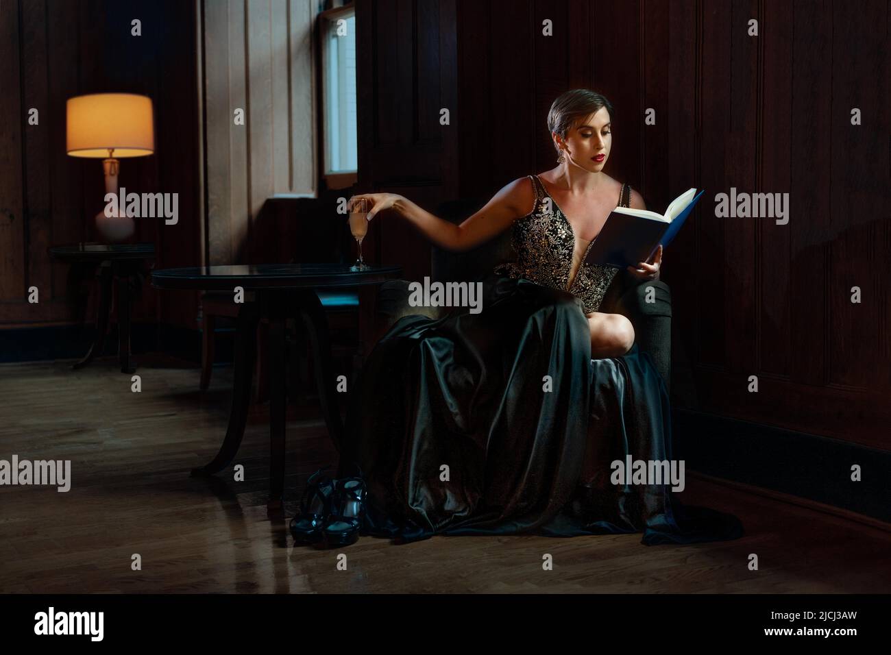 Eine junge Frau rutscht aus einer Party, um eine ruhige Ecke zu finden und ein Buch zu lesen. Sie ist introvertiert und entkommt den Massen und dem Lärm in diesem friedlichen Raum. Stockfoto