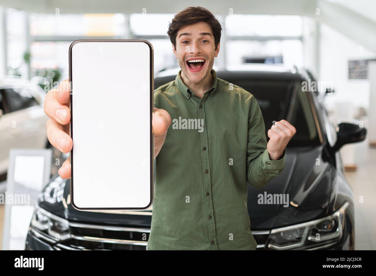 Mobiles Angebot. Emotionaler Junger Mann Mit Leerem Smartphone Im Auto-Showroom Stockfoto