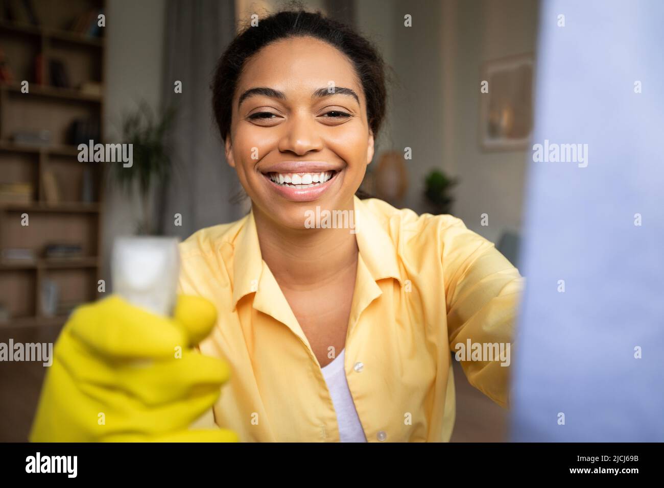 Fröhliche Afrikanische Dame Mit Waschmittel Spray Reinigungsfenster Zu Hause Stockfoto