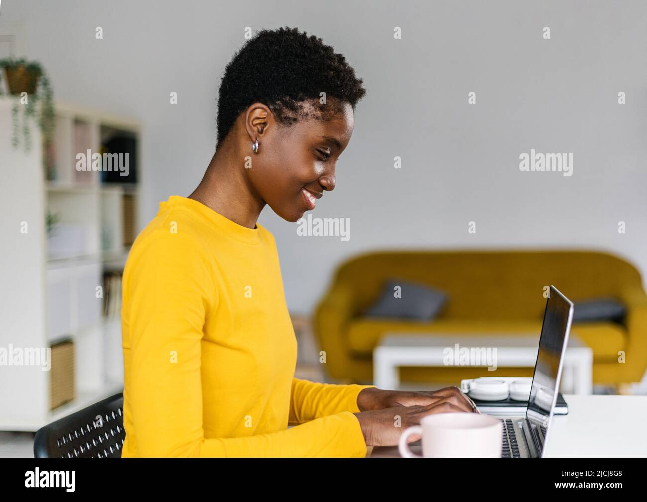 Lächelnde junge afrikanische Frau, die vom Heimbüro aus am Laptop arbeitet Stockfoto