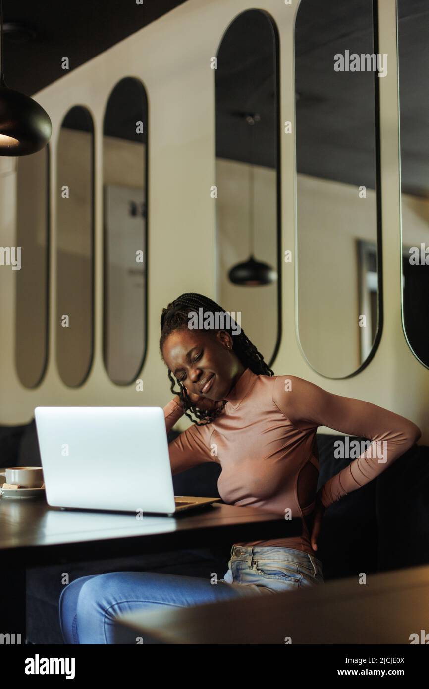 Vertikale verwirrt afro amerikanische Geschäftsfrau, Arbeit sitzen, fühlen sich ungesund in der Wirbelsäule in der Nähe Laptop im Café, Skoliose Problem Stockfoto