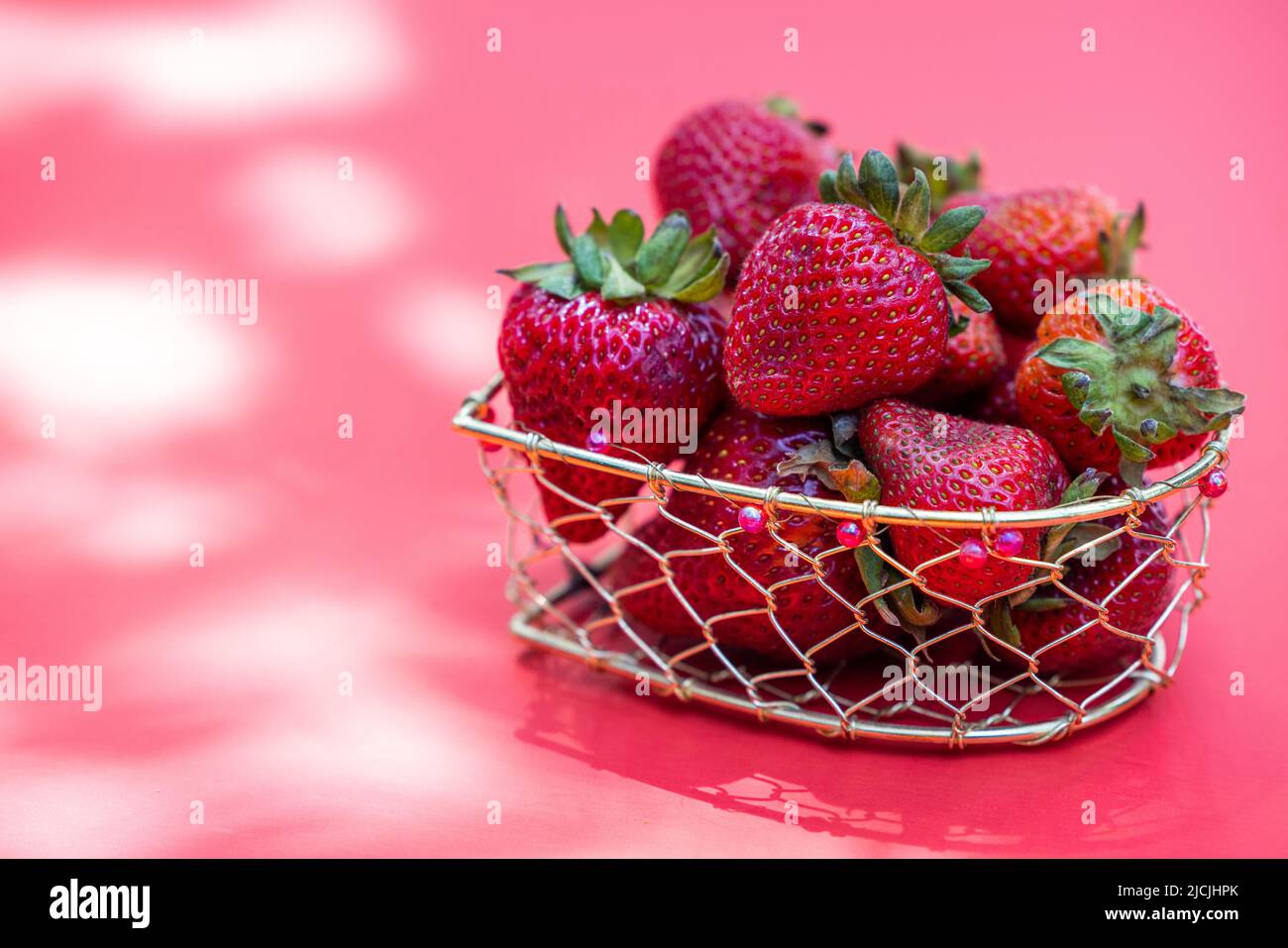 Leuchtend rote Erdbeeren in einem Drahtkorb auf weißem Hintergrund Stockfoto