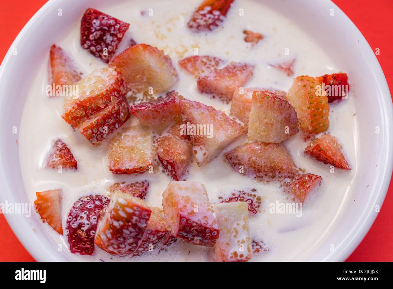 Frische Erdbeeren mit schwerer Rahm und einem Spritzer Zucker auf rotem Hintergrund Stockfoto