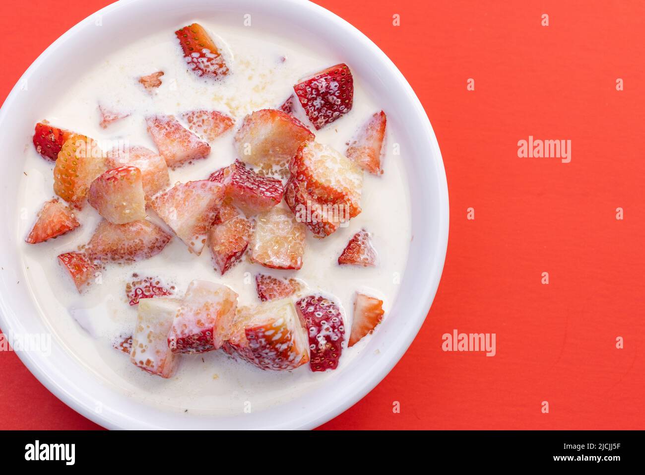 Frische Erdbeeren mit schwerer Rahm und einem Spritzer Zucker auf rotem Hintergrund Stockfoto