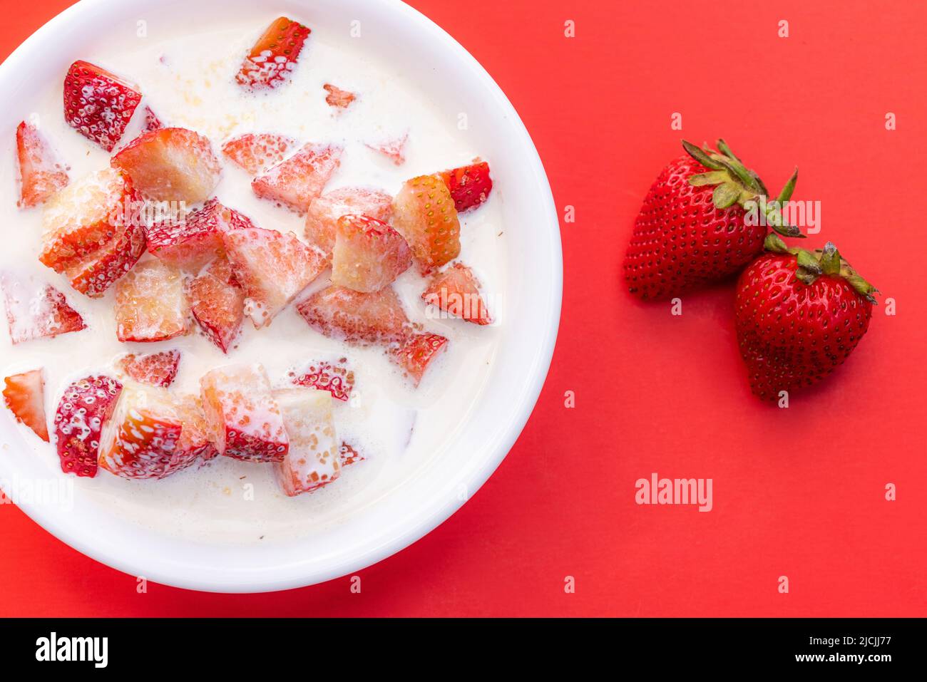 Frische Erdbeeren mit schwerer Rahm und einem Spritzer Zucker auf rotem Hintergrund Stockfoto