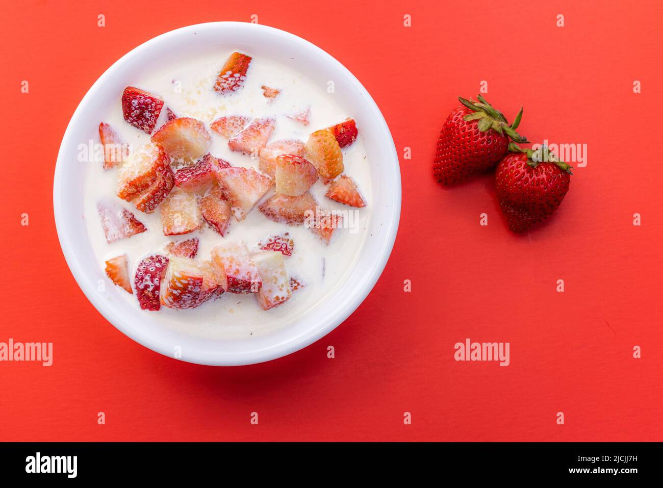 Frische Erdbeeren mit schwerer Rahm und einem Spritzer Zucker auf rotem Hintergrund Stockfoto