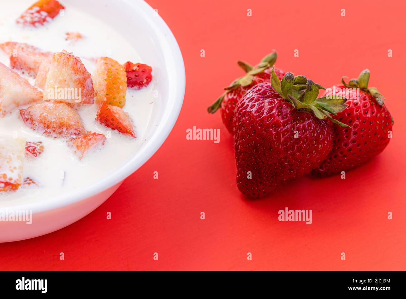 Frische Erdbeeren mit schwerer Rahm und einem Spritzer Zucker auf rotem Hintergrund Stockfoto
