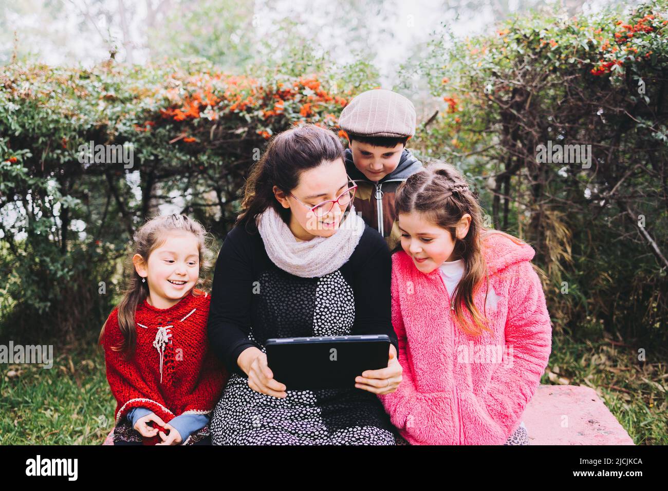 Alleinerziehende Mutter mit ihrem Sohn und ihren Töchtern, die ein Tablet benutzen, um sich einen Film im Park anzusehen. Lateinische alleinerziehende Familie Stockfoto