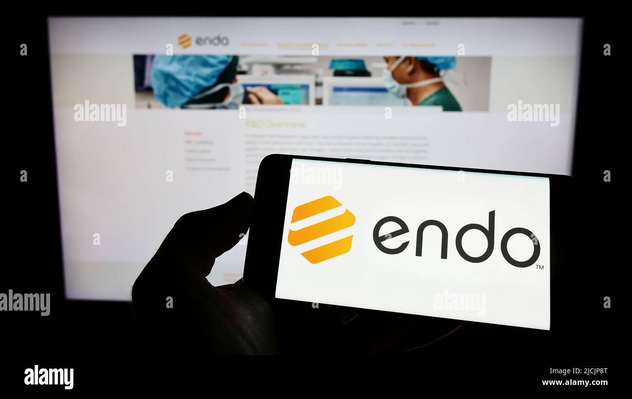 Person mit Mobiltelefon und Logo des Pharmaunternehmens Endo International plc auf dem Bildschirm vor der Webseite. Konzentrieren Sie sich auf die Telefonanzeige. Stockfoto