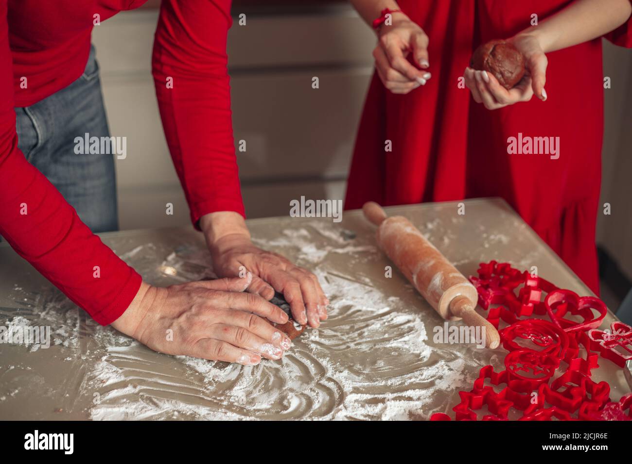 Hausgemachtes Backkonzept, Hände von unkenntlichen Männern und Frauen, die Kekse kochen. Backen zu Hause. Rote Kleidung. Weihnachten. Glück, gemütliches Zuhause, Stockfoto