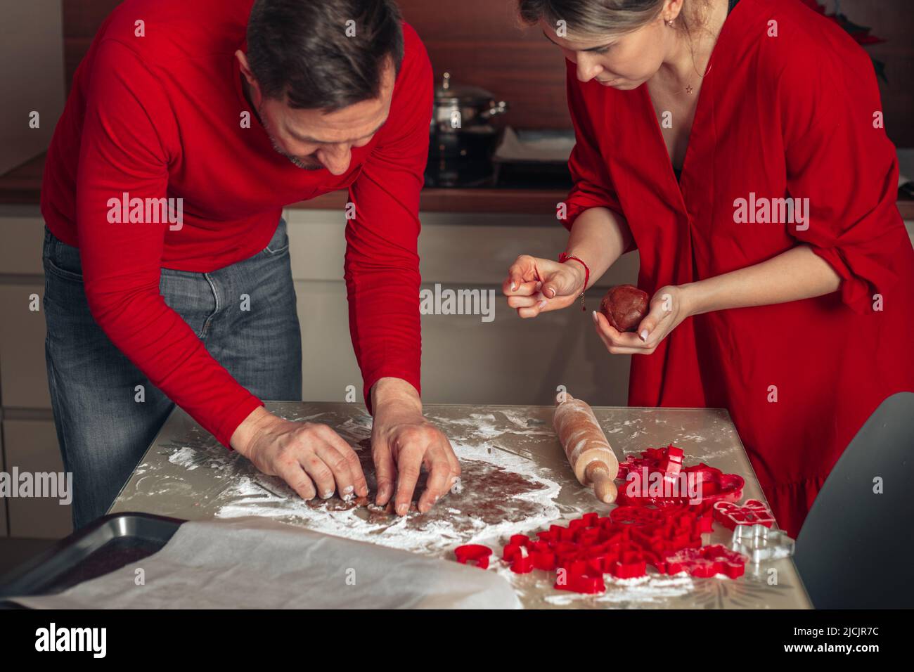 Das junge Paar lehnte sich über den Tisch, um Kekse zu schneiden. Weihnachten glückliche Momente, Mann und Frau kochen zu Hause. Teig auf dem Tisch. Gemütliche Küche zu Hause und Glück Stockfoto