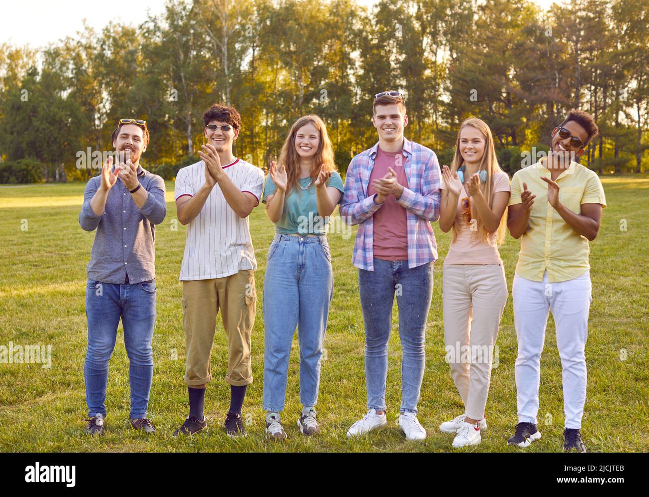 Fröhliche junge weibliche und männliche Freunde applaudieren zusammen während des Sommerspaziergangs im Park. Stockfoto