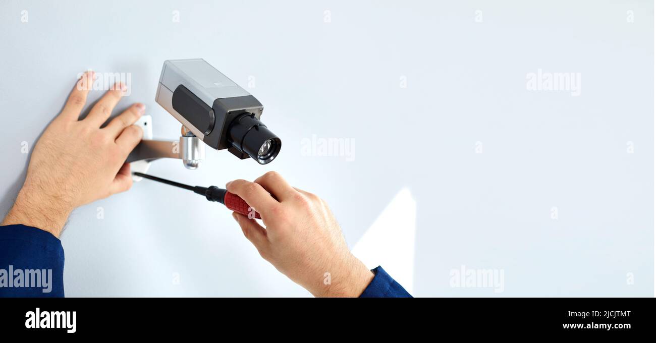 Nahaufnahme der Hände eines männlichen Arbeiters, der mit einem Schraubendreher die cctv-Kamera an einer weißen Wand befestigt. Stockfoto