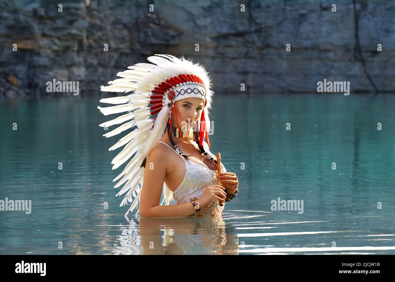 Ein Mädchen wird in einem Steinbruch als Indianerin der Ureinwohner Amerikas gesehen. Sie ist ganz in Weiß gekleidet und trägt einen weißen Kopfschmuck mit Federn. Sie wird beim Flötenspielen gesehen Stockfoto