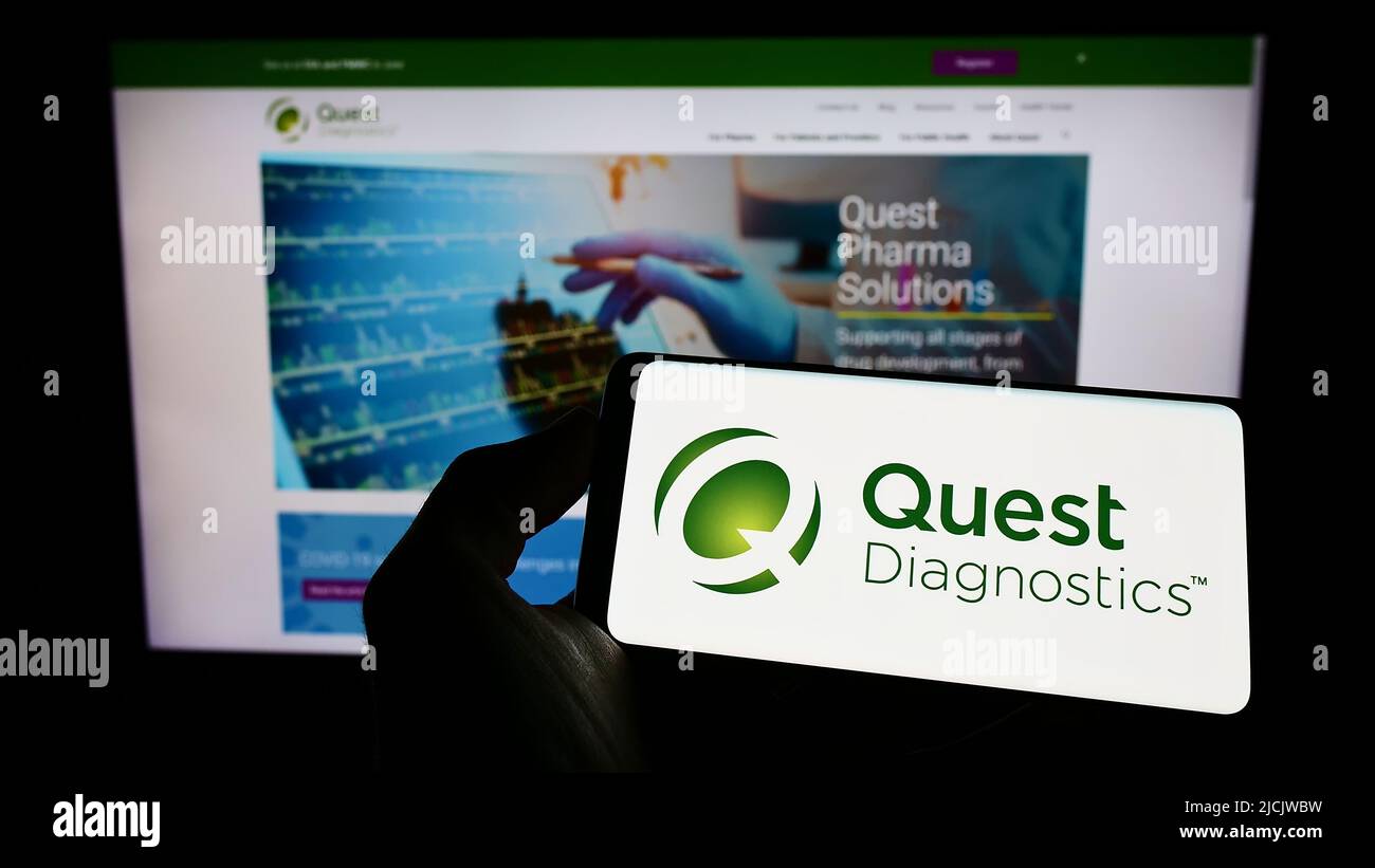 Person mit Mobiltelefon und Logo des US-Laborunternehmens Quest Diagnostics Inc. Auf dem Bildschirm vor der Webseite. Konzentrieren Sie sich auf die Telefonanzeige. Stockfoto