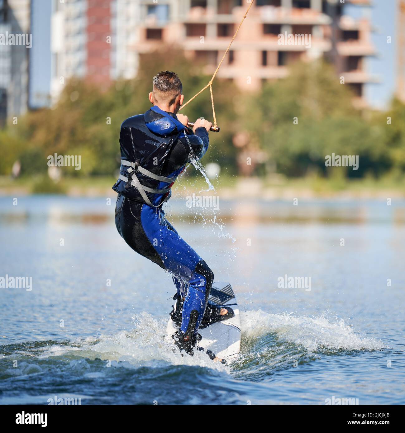 Rückansicht des Wakeboarder-Surfens am See. Junger Surfer, der Spaß beim Wakeboarden im Seilpark hat. Wassersport, Outdoor-Aktivitätskonzept. Stockfoto