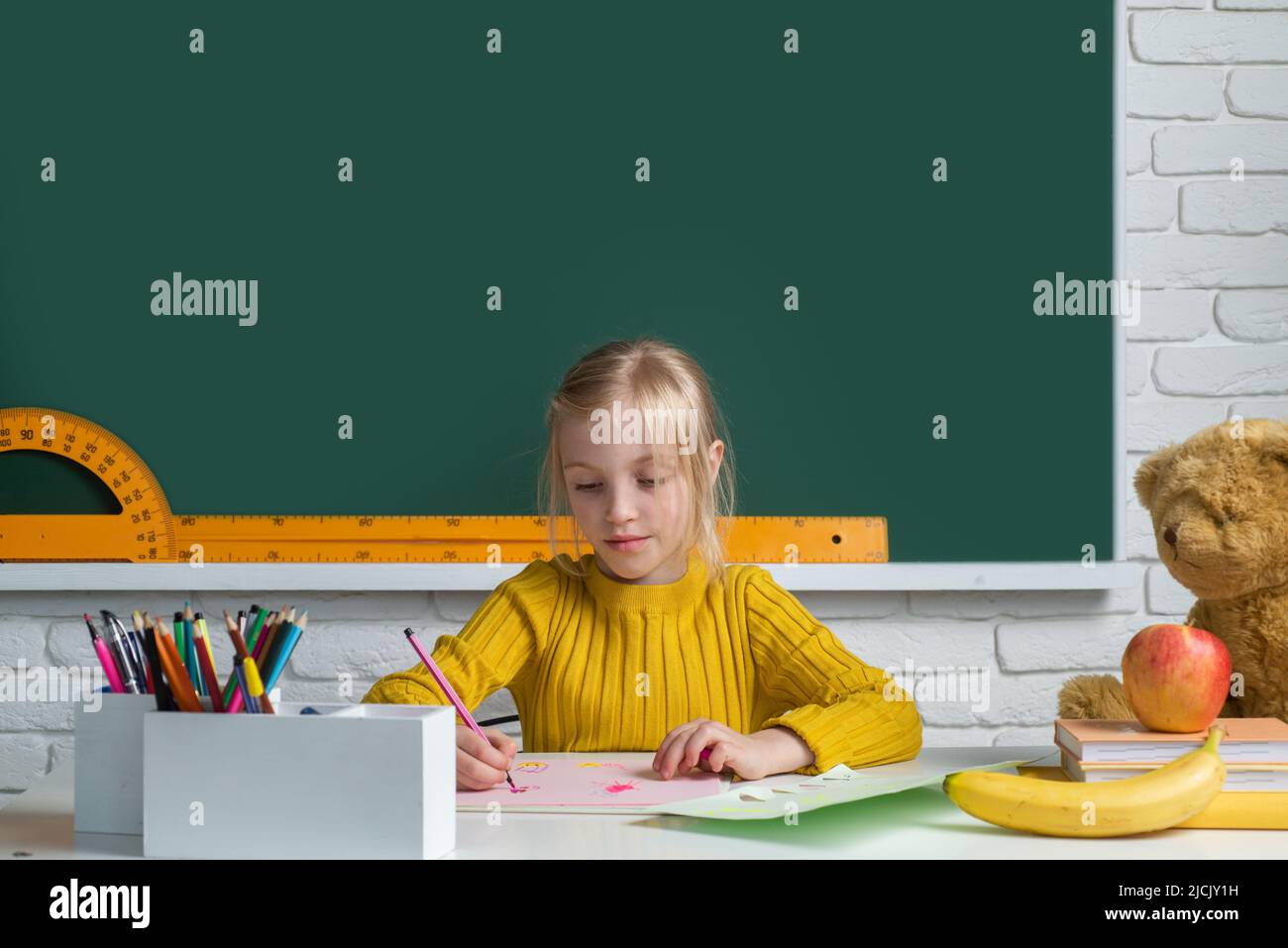 Schulmädchen lernen Lektion sitzen am Schreibtisch Lernen auf Klassenzimmer Tafel Hintergrund. Bildung, Lernen und Kinderkonzept. Stockfoto