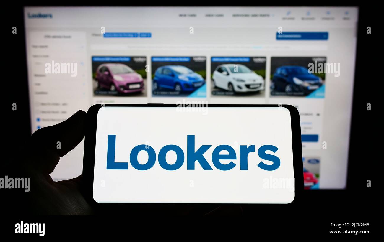 Person, die das Smartphone mit dem Logo des britischen Autohandels Lookers plc auf dem Bildschirm vor der Website hält. Konzentrieren Sie sich auf die Telefonanzeige. Stockfoto