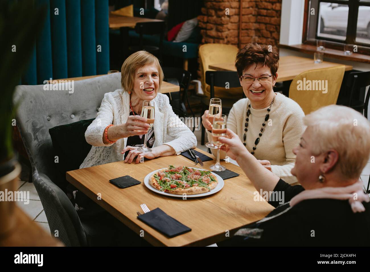 Drei ältere Freundinnen beim Abendessen im Restaurant mit Pizza und Wein, attraktive Dame verbringen Zeit zusammen drinnen. Alte Freunde feiern Stockfoto