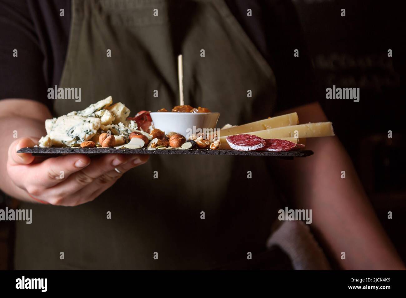Kellnerin hält schwarzes Steinbrett mit Delikatessen. Stockfoto