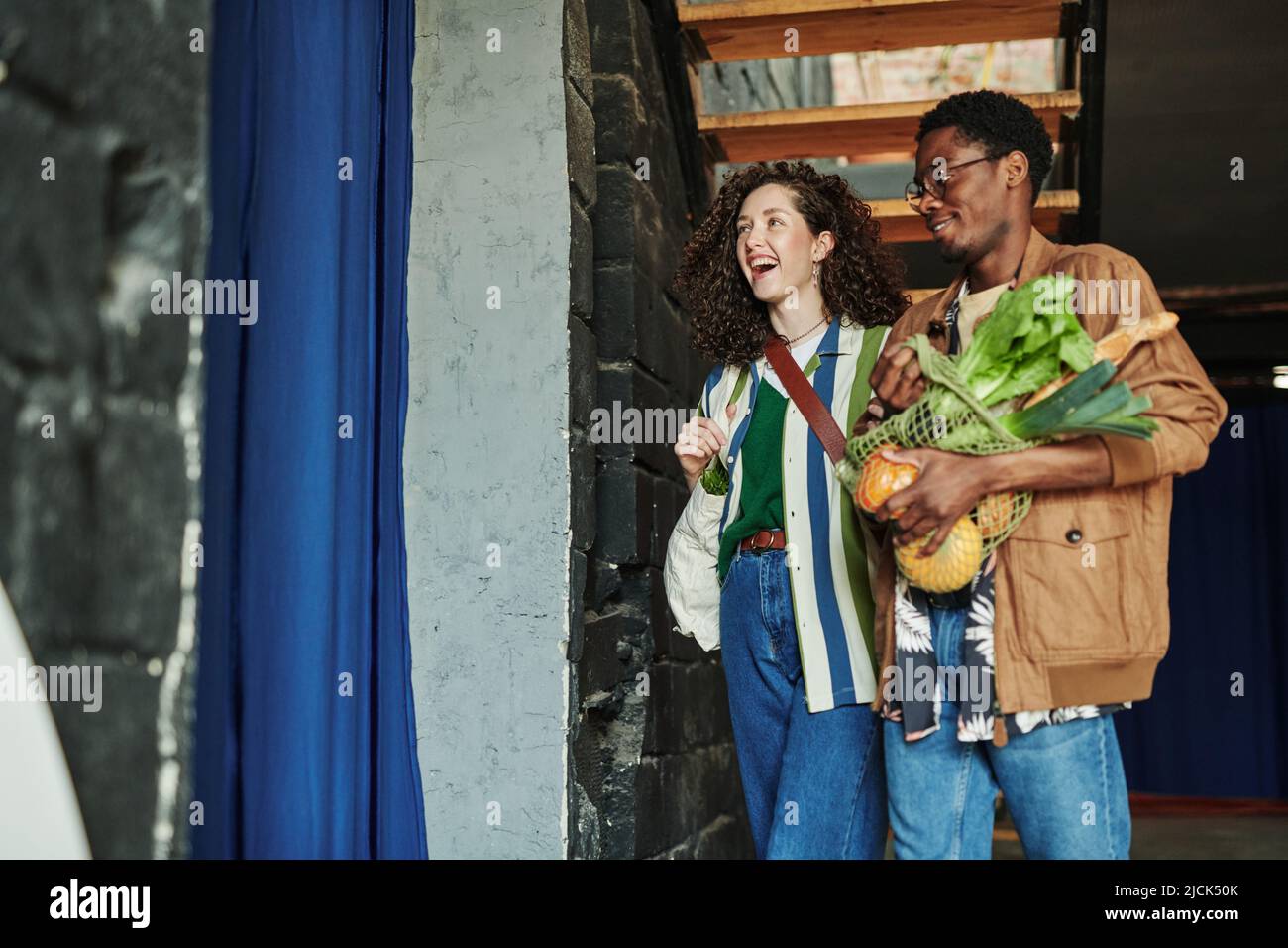 Junge, fröhliche Vegetarier kommen aus dem Supermarkt zurück, wo sie frisches Gemüse gekauft haben Stockfoto