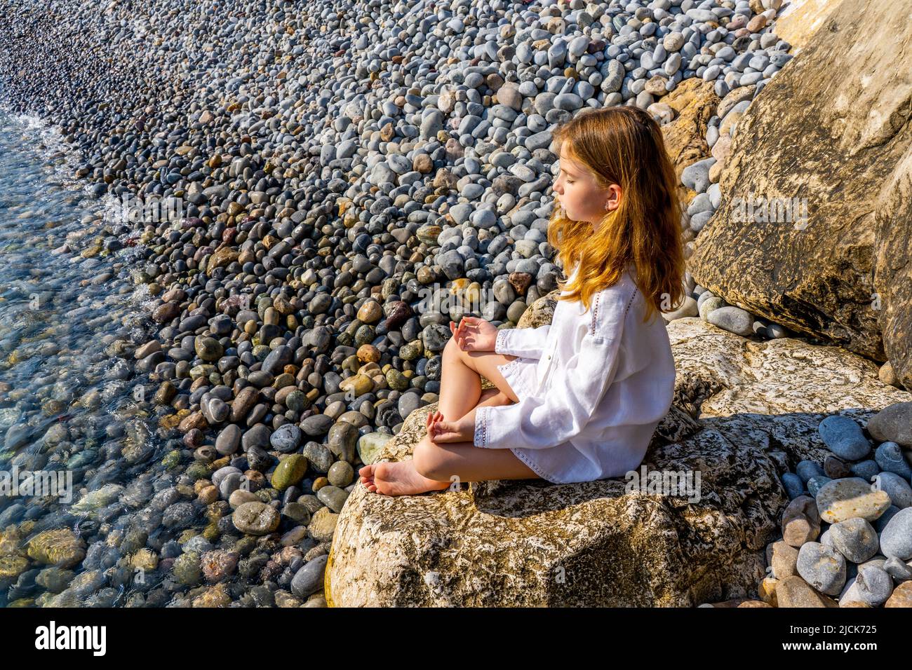 Schönes kleines Mädchen, das auf einem Felsen am Meer sitzt und meditiert. Hochwertige Fotos Stockfoto