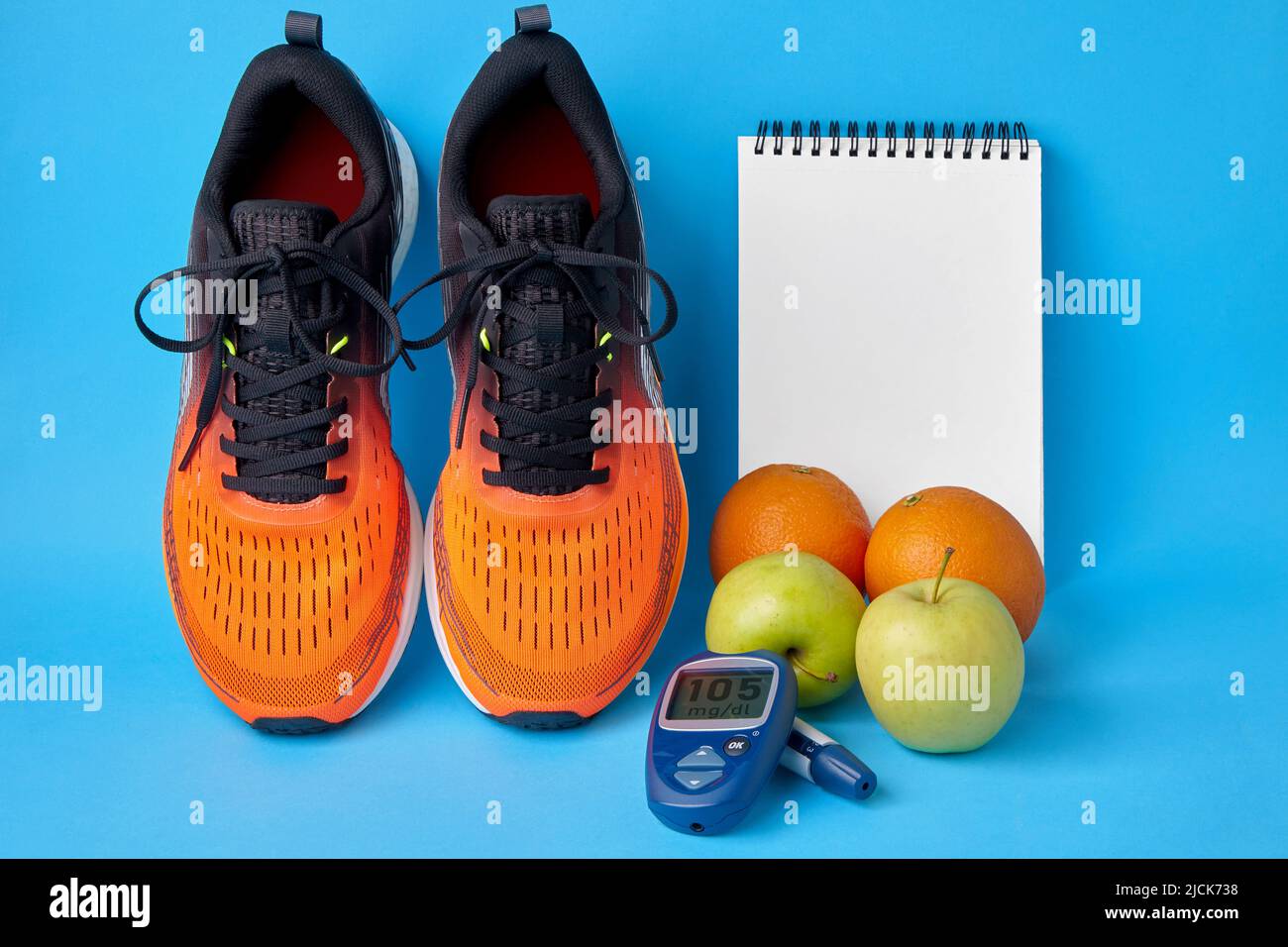 Orangefarbene Sneakers, Notizblock, Glucometer und Obst auf blauem Hintergrund. Gesundes Lebensstilkonzept zur Aufrechterhaltung eines normalen Blutzuckerspiegels. Insulinresistenz Stockfoto