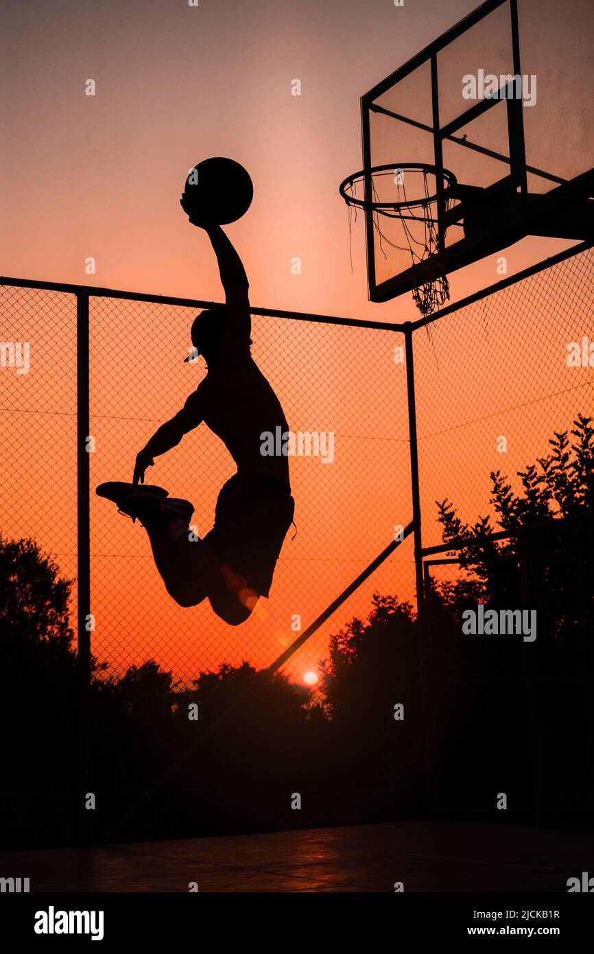 Basketball-Spieler erzielte einen erstaunlichen Slam Dunk im Freien. Wunderschöne Aussicht auf den Sonnenuntergang. Sonnenleuchten. Stockfoto