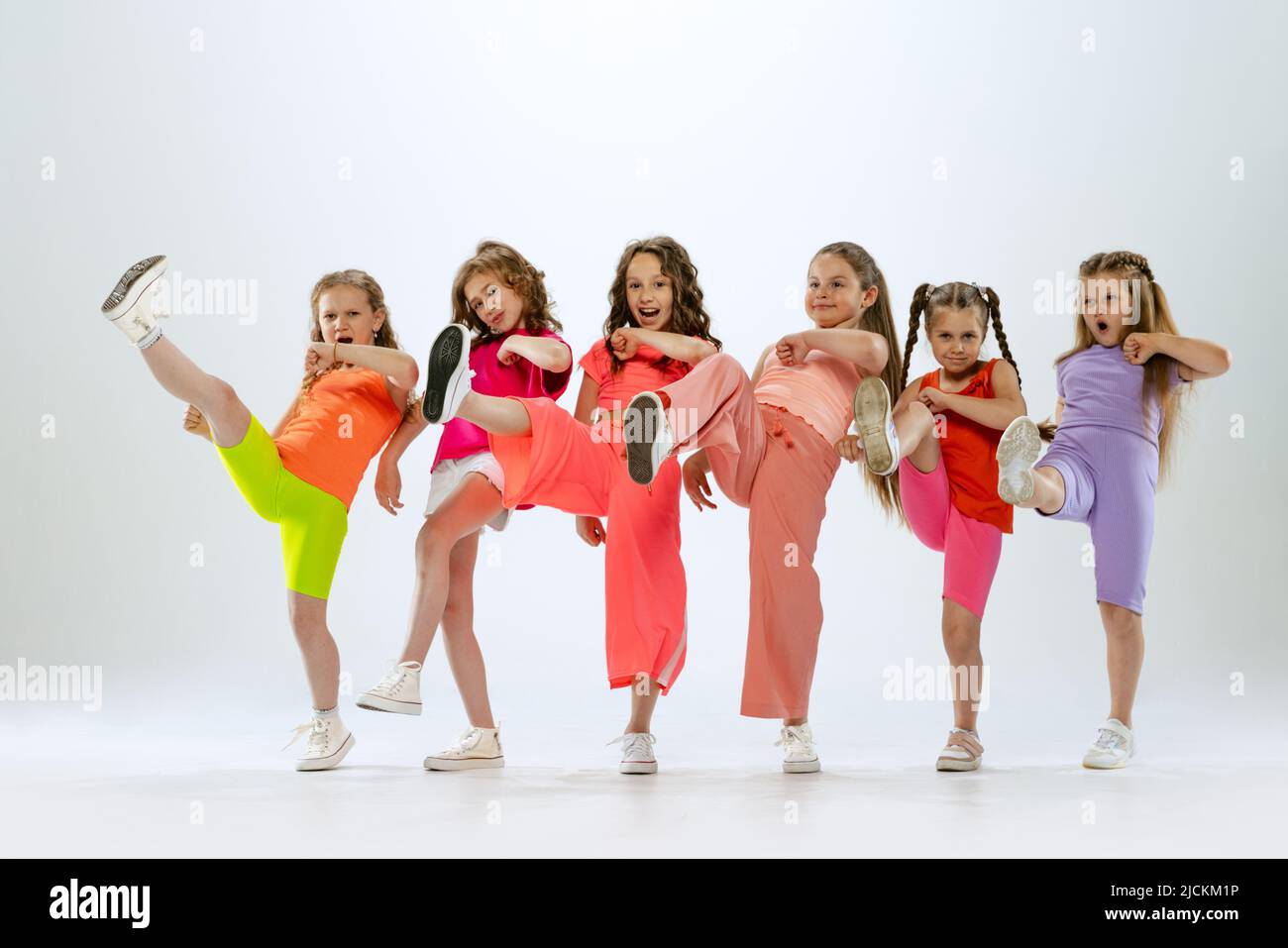 Tanzgruppe von glücklichen, aktiven kleinen Mädchen in hellen bunten Kleidern tanzen isoliert auf weißem Studiohintergrund. Konzept von Musik, Mode, Kunst Stockfoto