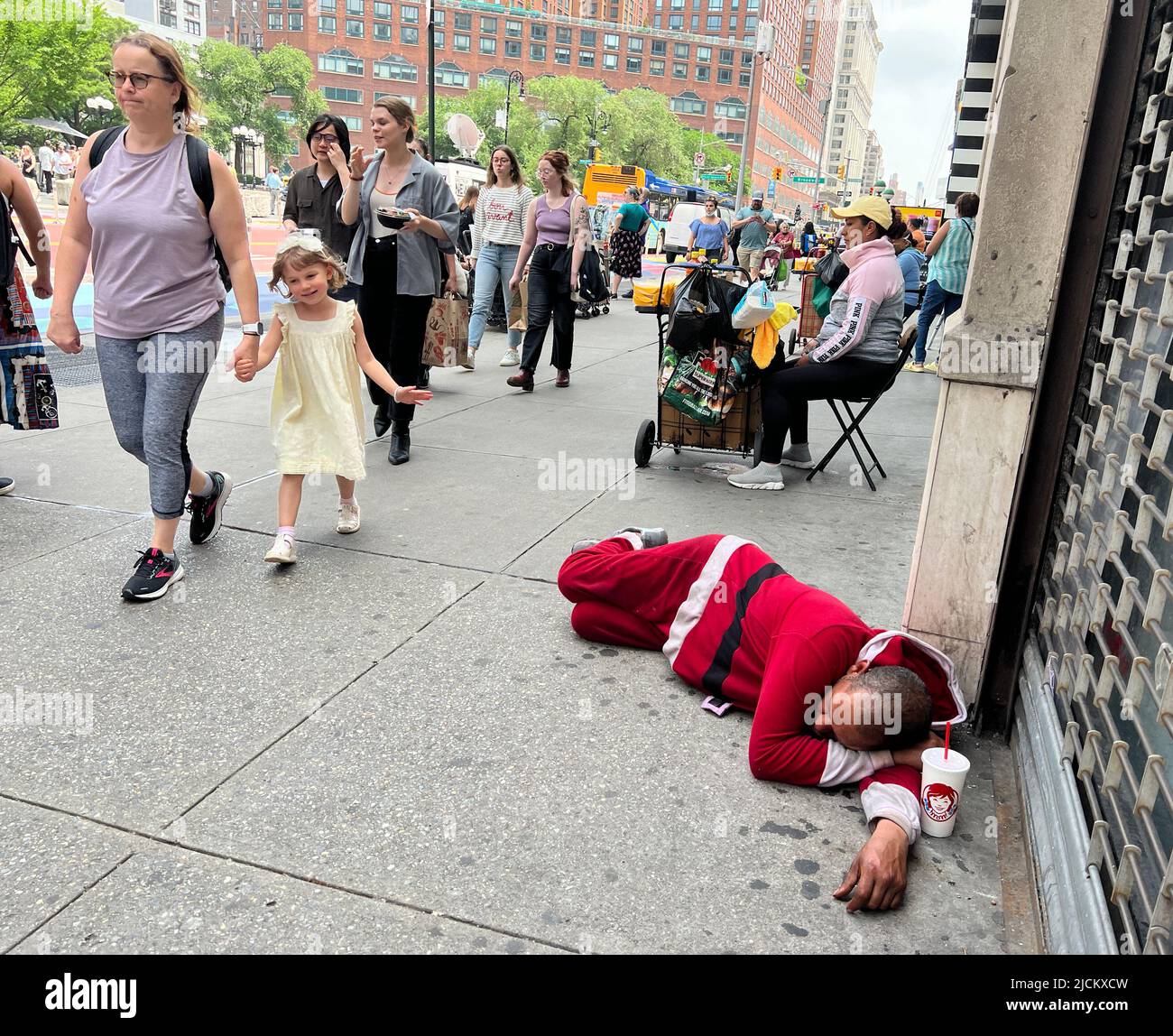 Der Mann schläft in einem Weihnachtsanzug auf dem Bürgersteig in der 14. Street gegenüber vom Union Square, während die Leute an einem warmen Frühlingstag vorbeikommen. Manhattan, New York City. Stockfoto