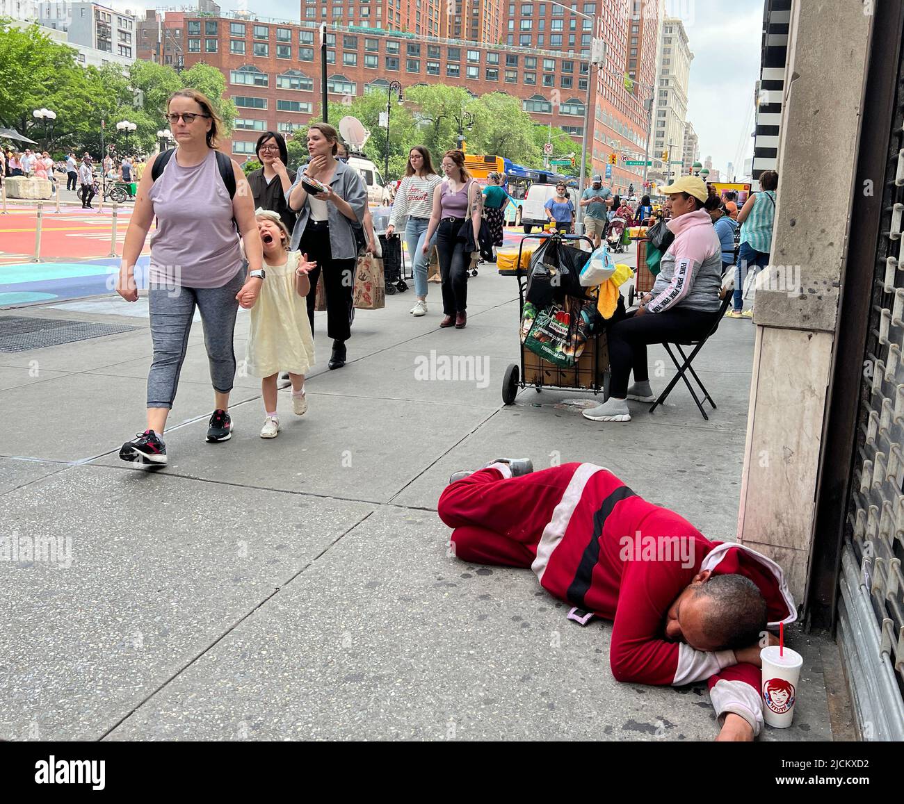 Der Mann schläft in einem Weihnachtsanzug auf dem Bürgersteig in der 14. Street gegenüber vom Union Square, während die Leute an einem warmen Frühlingstag vorbeikommen. Manhattan, New York City. Stockfoto