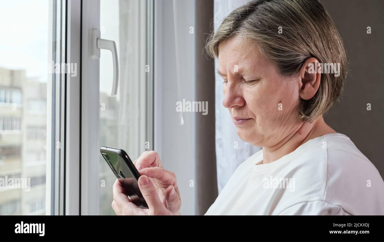 Die alte Frau scrollt auf dem schwarzen Smartphone durch Webseiten Stockfoto