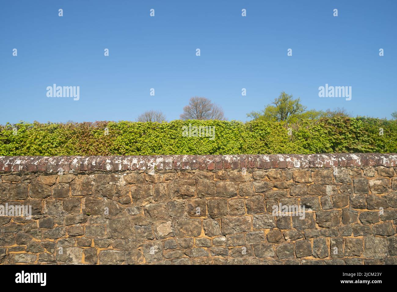 Kentish Ragstone ein harter grauer Kalkstein, der verwendet wurde, um eine starke Grenzmauer mit roten Ziegelsteinen zu errichten, die oben gegen einen blauen Himmel stehen Stockfoto