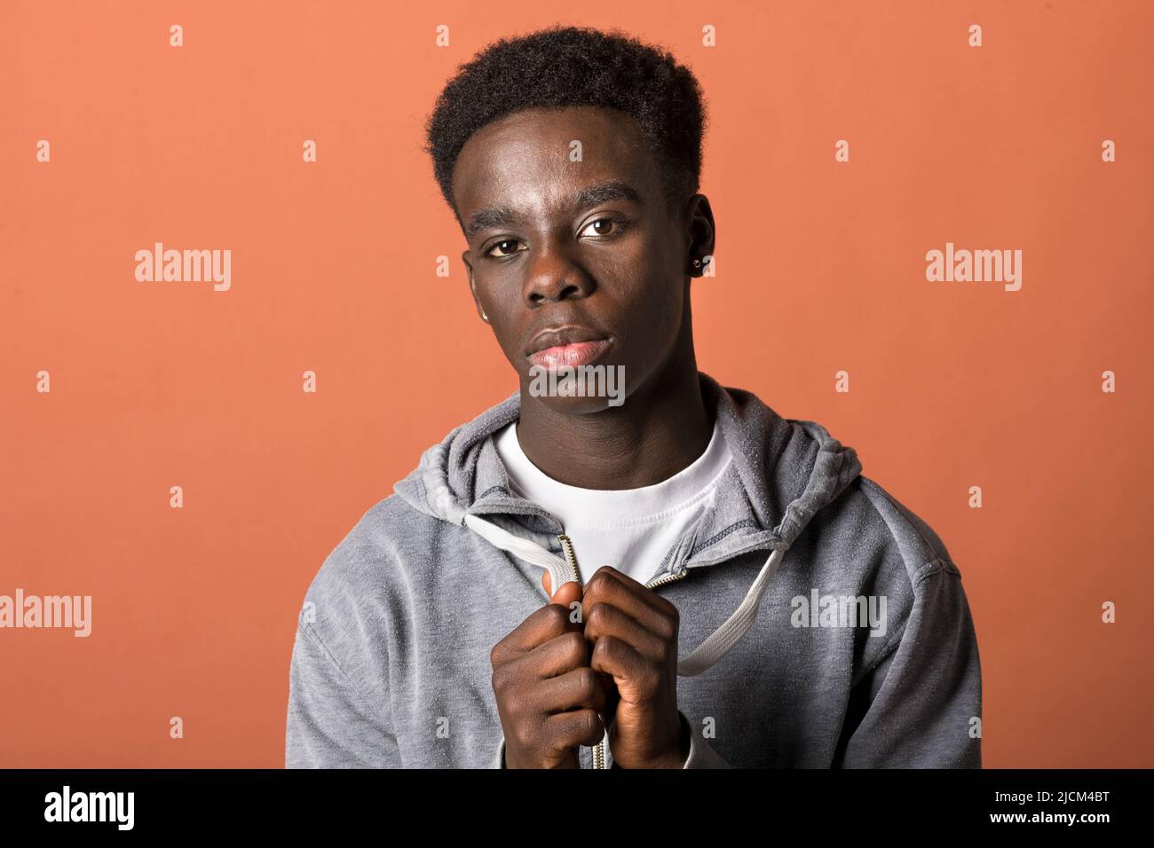 Isolierter junger afroamerikanischer Rüde im Kapuzenpullover, der die Kamera anschaut, sich die Hände anschließt und vor braunem Hintergrund um etwas bettelt Stockfoto