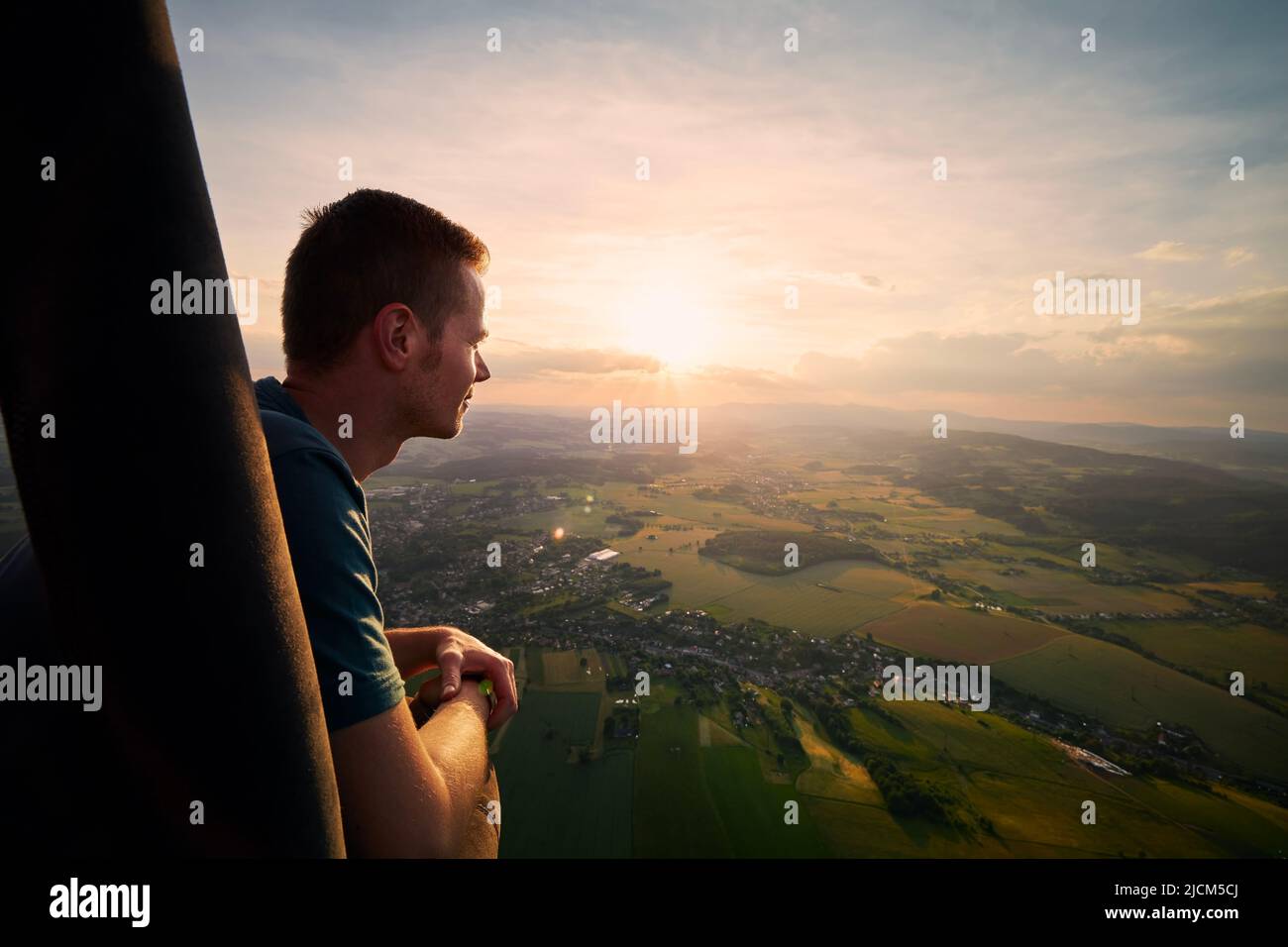 Mann, der den Blick vom Heißluftballon während des Fluges über die wunderschöne Landschaft bei Sonnenuntergang genießt. Themen Abenteuer, Freiheit und Reisen. Stockfoto