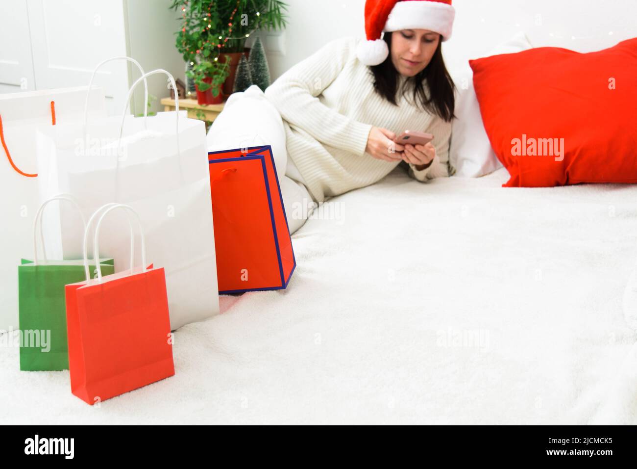 Schöne lächelnde Frau in Santa Hut hält Telefon und Bank Plastikkarte Stockfoto