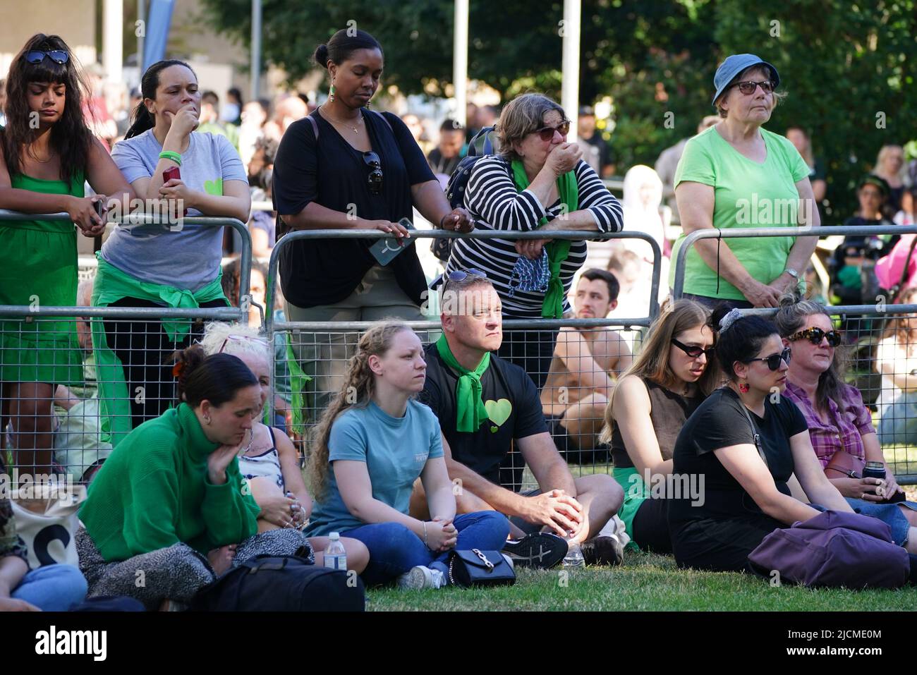 Auf einer Großleinwand am Fuß des Grenfell Tower in London beobachten die Menschen eine Zeremonie zur Festlegung von Glaubensbekenntnis und Kranz, um an die zu erinnern, die am 14 2018. Juni beim Feuer im Grenfell Tower ums Leben kamen. Bilddatum: Dienstag, 14. Juni 2022. Stockfoto