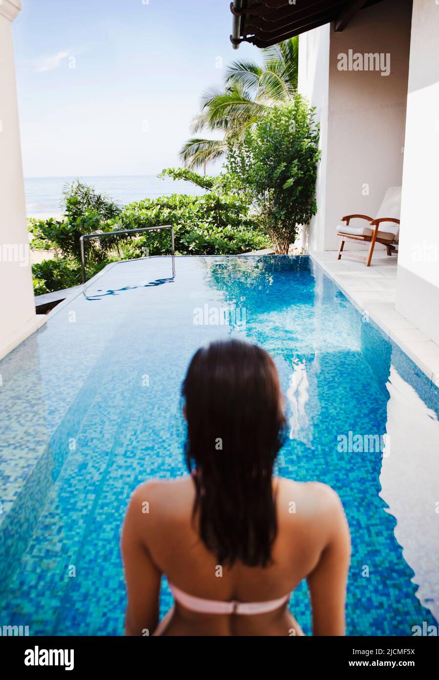 Eine Frau kommt in den privaten Pool mit Meerblick der Grand Deluxe Villa in Saman Villas, Aturuwella, Bentota, Sri Lanka. Stockfoto