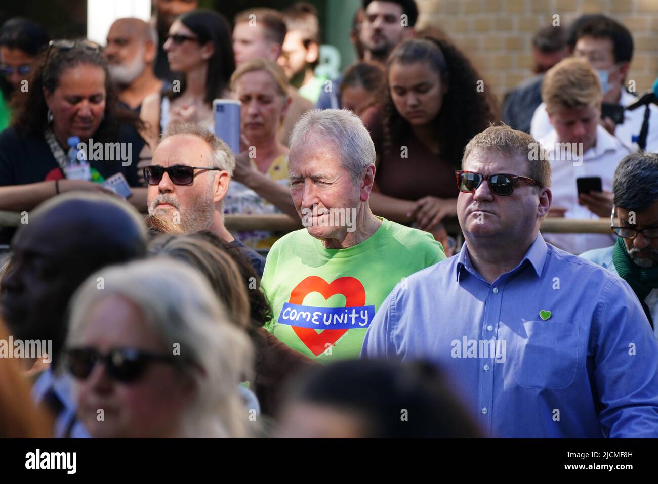 Auf einer Großleinwand am Fuß des Grenfell Tower in London beobachten die Menschen eine Zeremonie zur Festlegung von Glaubensbekenntnis und Kranz, um an die zu erinnern, die am 14 2018. Juni beim Feuer im Grenfell Tower ums Leben kamen. Bilddatum: Dienstag, 14. Juni 2022. Stockfoto