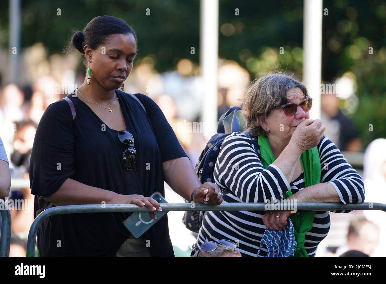 Auf einer Großleinwand am Fuß des Grenfell Tower in London beobachten die Menschen eine Zeremonie zur Festlegung von Glaubensbekenntnis und Kranz, um an die zu erinnern, die am 14 2018. Juni beim Feuer im Grenfell Tower ums Leben kamen. Bilddatum: Dienstag, 14. Juni 2022. Stockfoto