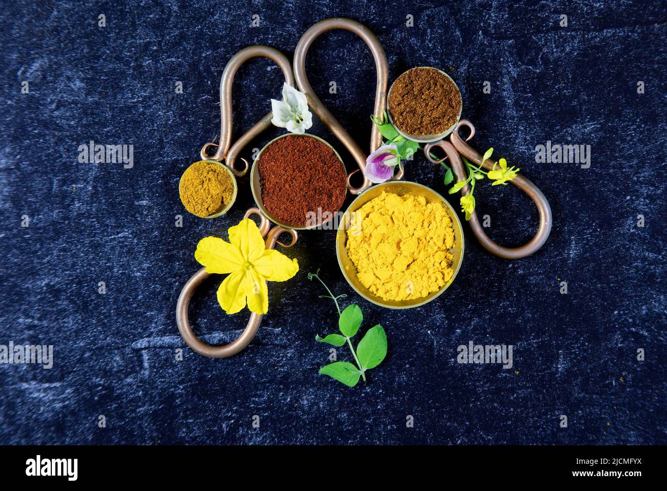 Vintage Metalllöffel mit gemahlenen Gewürzen aus Chilipulver, Tumeric, Paprika und Kurvepulver mit frischen Blumen aus blühendem Gemüse auf schwarz mit Stockfoto