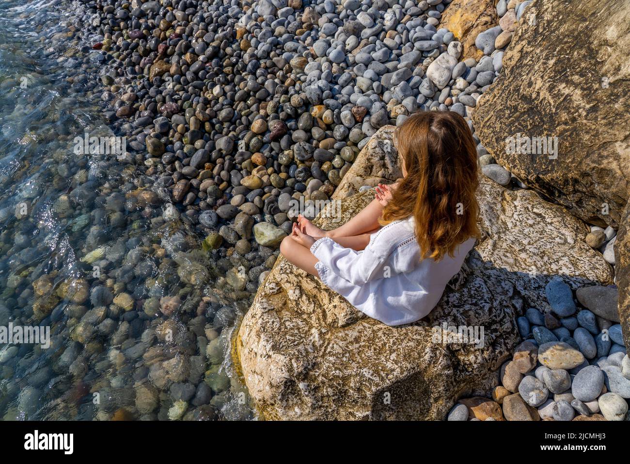 Schönes kleines Mädchen, das auf einem Felsen am Meer sitzt und meditiert. Hochwertige Fotos Stockfoto