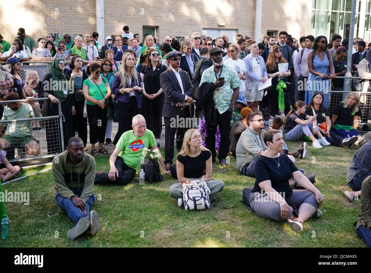 Auf einer Großleinwand am Fuß des Grenfell Tower in London beobachten die Menschen eine Zeremonie zur Festlegung von Glaubensbekenntnis und Kranz, um an die zu erinnern, die am 14 2018. Juni beim Feuer im Grenfell Tower ums Leben kamen. Bilddatum: Dienstag, 14. Juni 2022. Stockfoto