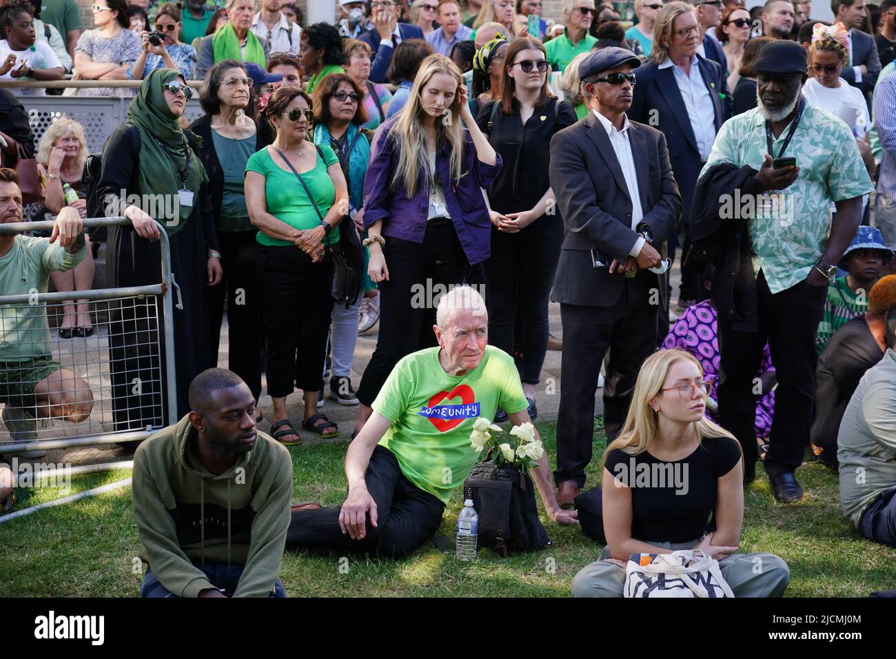 Auf einer Großleinwand am Fuß des Grenfell Tower in London beobachten die Menschen eine Zeremonie zur Festlegung von Glaubensbekenntnis und Kranz, um an die zu erinnern, die am 14 2018. Juni beim Feuer im Grenfell Tower ums Leben kamen. Bilddatum: Dienstag, 14. Juni 2022. Stockfoto