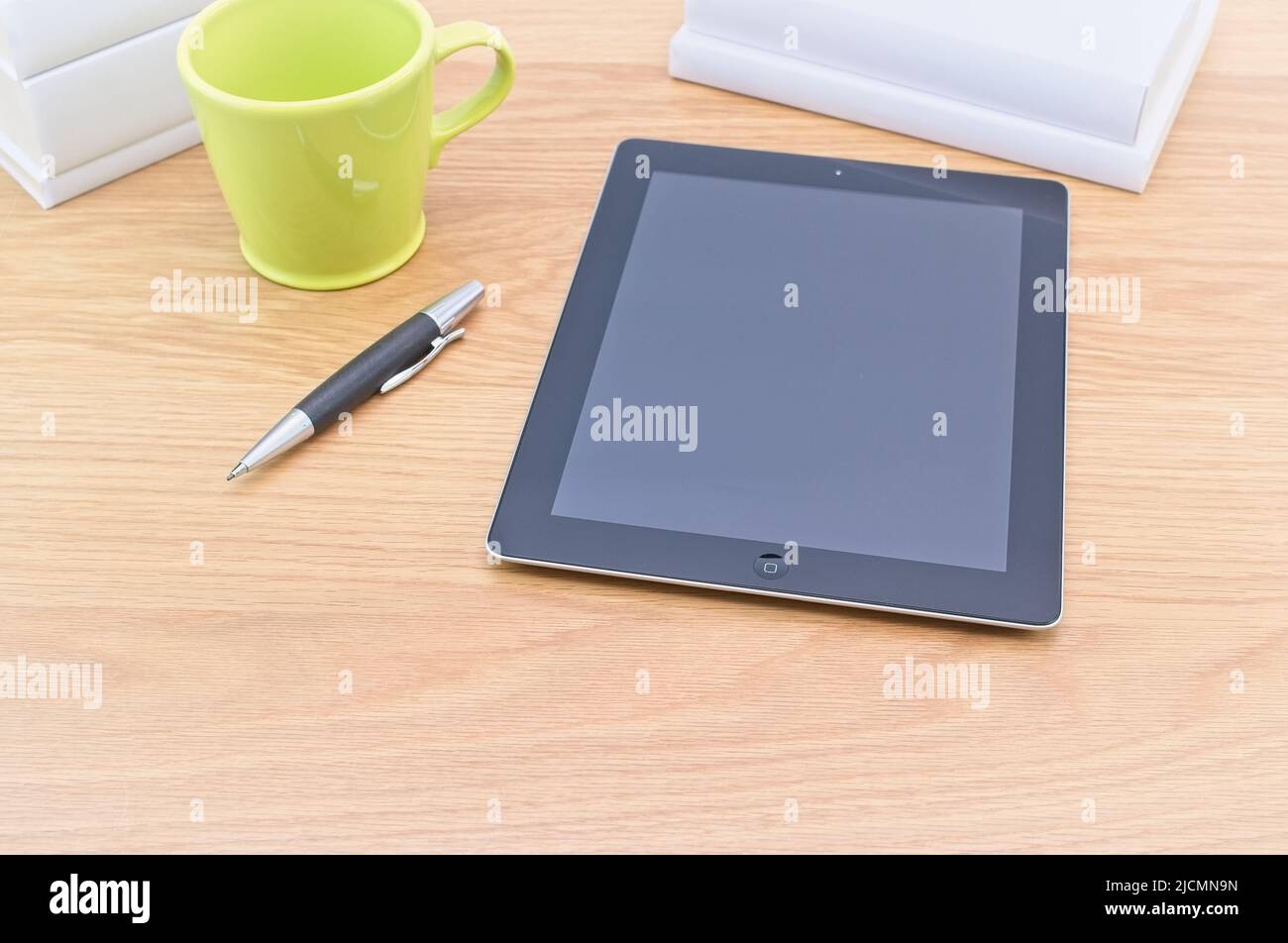 Apple ipad Tablet mit Bücher Stift und Becher auf einem hellen Holztisch an der weißen Wand Stockfoto