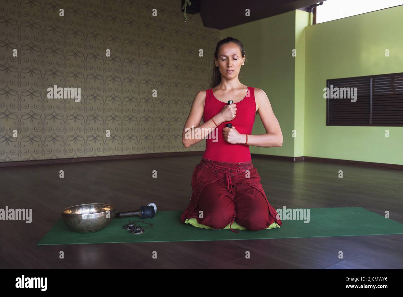 Eine Frau meditiert mit Gegenständen in ihren Händen und verschiedenen Räucherstäbchen, die auf einer Matte im Raum sitzen Stockfoto