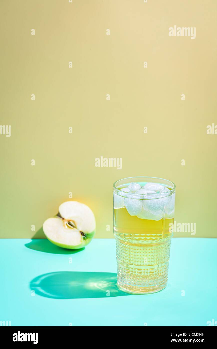 Glas Apfelsaft mit Eis auf gelbem Hintergrund, helle Schatten Stockfoto