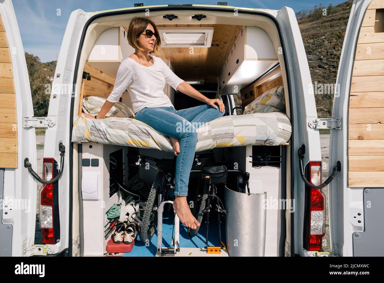 Konzept: Vanlife. Abenteuerliches Mädchen, das im Wohnmobil sitzt, mit offenen Türen und Blick auf die Landschaft. Mit Fahrrädern im Kofferraum. Stockfoto